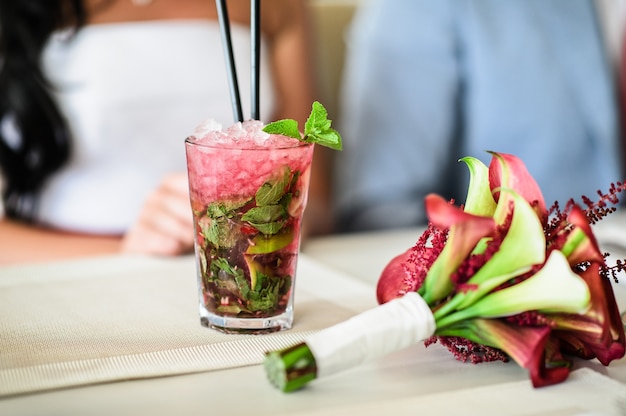 The bride is holding a glass of Mojito, wedding bouquet on the table in the restaurant