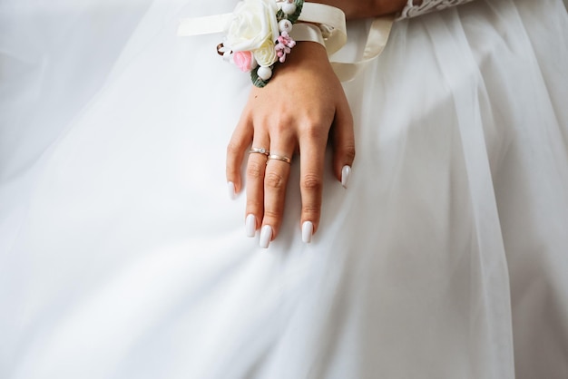 Bride is holding hands on knees Beautiful white manicure Engagement rings on fingers Wedding day details Elegant accessories