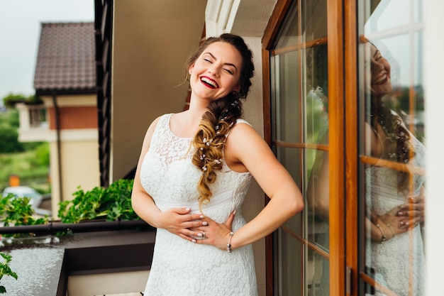 The bride is standing on the balcony and smiles genuinely She closed her eyes and holding hands on waist