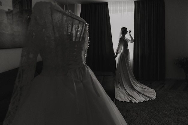 A bride is standing in front of a dresser with a white dress on