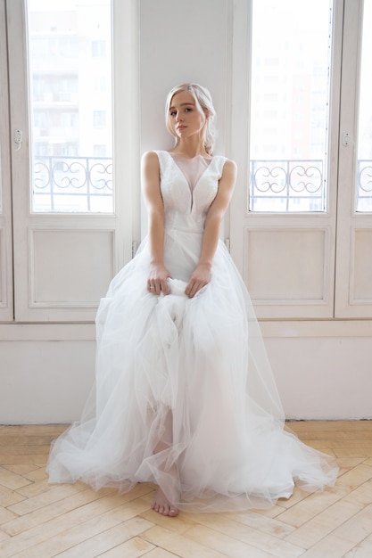 Bride is a woman in a light summer wedding dress standing at the window