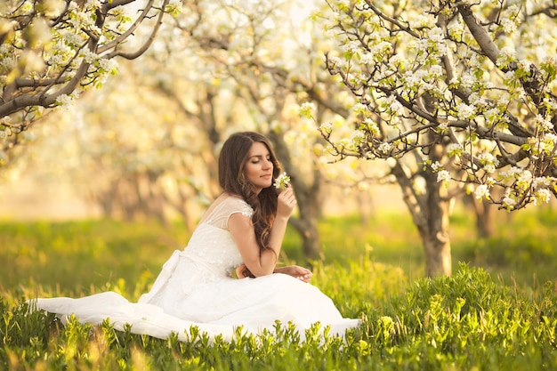 Bride in ivory wedding dress with long curly hair sitting in spring gardens with blossom trees