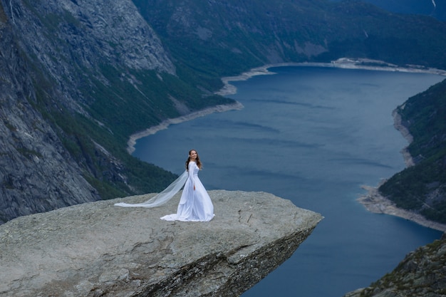 노르웨이의 산에서 Trolltunga 바위의 조각에 긴 웨딩 드레스의 신부