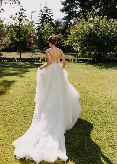 Bride in a long white dress running away on green grass