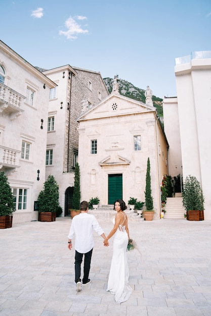 Photo bride looks back as she walks with groom to the church of st sava perast montenegro back view