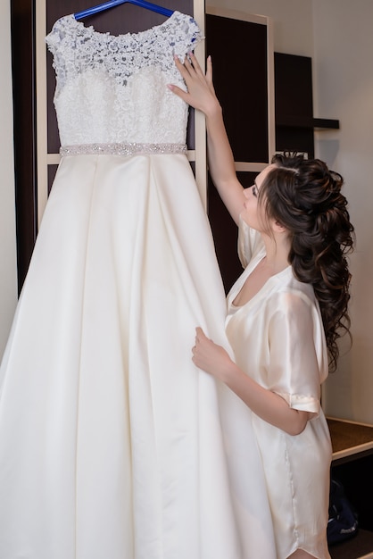 Photo the bride looks at the wedding dress which hangs on the hanger