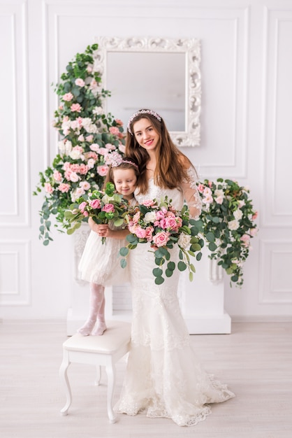 Bride mother and daughter in white dresses with flowers.