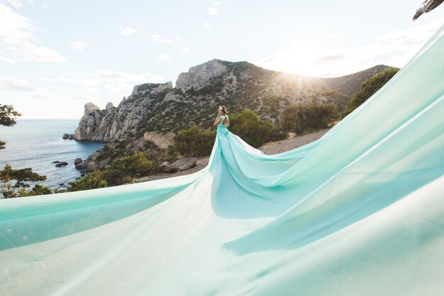 Sposa in natura in montagna vicino all'acqua. colore del vestito tiffany. la sposa sta giocando con il suo vestito.