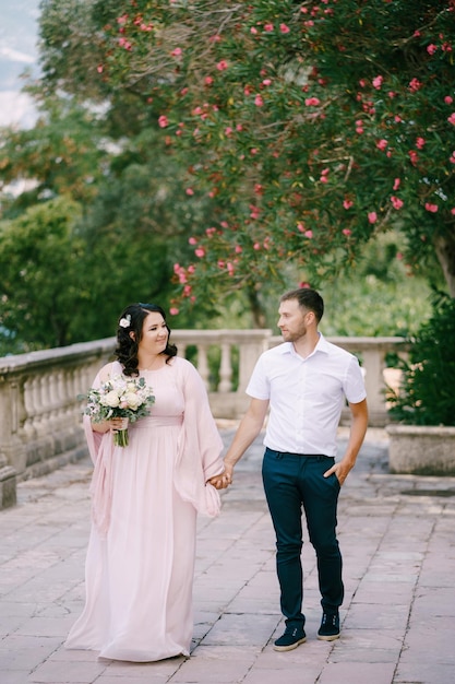 La sposa in un vestito rosa con un bouquet tiene la mano dello sposo