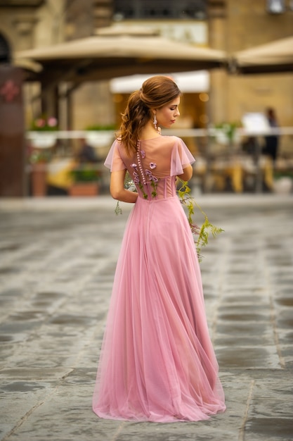 Photo a bride in a pink dress with a bouquet stands in the center of the old city of florence in italy.