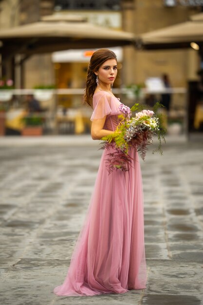 꽃다발과 함께 분홍색 드레스를 입은 신부는 이탈리아 피렌체의 구시 가지 중심에 서 있습니다.