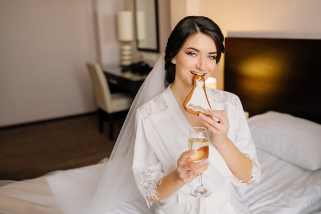 Bride portrait at wedding morning. Bride eating wedding gingerbread and holds a glass of champagne.