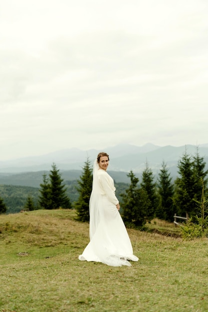 Bride portrait A young girl in a white wedding dress and with a bouquet of flowers and greenery in her hands against the backdrop of mountains and forests at sunset