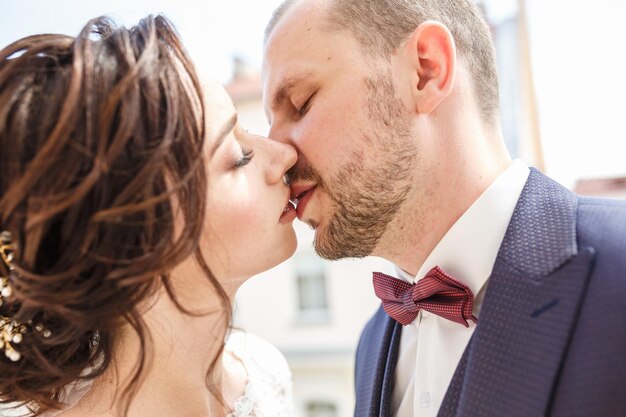 La sposa mette le mani sulle spalle dello sposo sposa con un bouquet di rose bianche e rosse abbraccia e bacia lo sposo