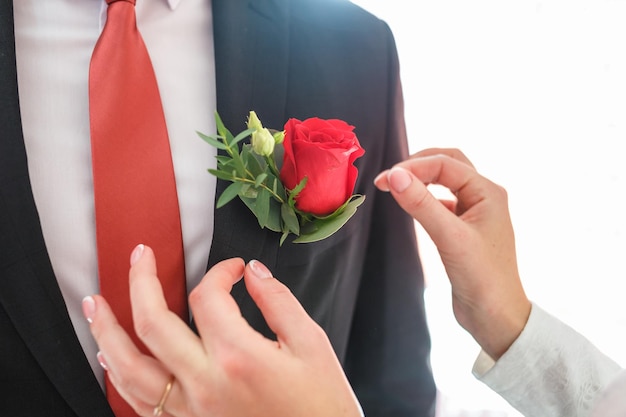 Bride puts groom on boutonniere from red rose on wedding day