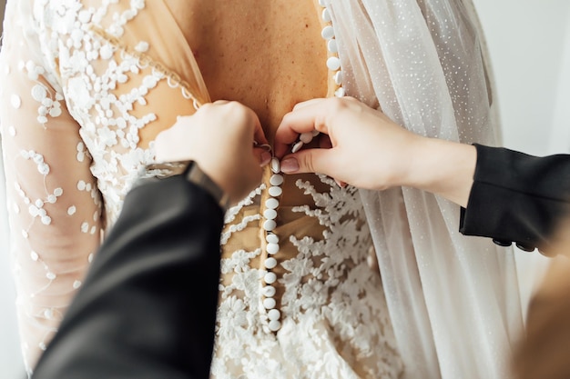 The bride puts on a white lace wedding dress mom and girlfriend of the bride help to tie the dress from the back