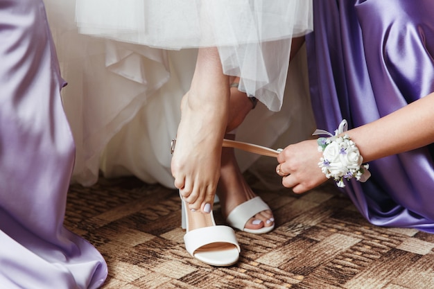 the bride puts on white wedding shoes