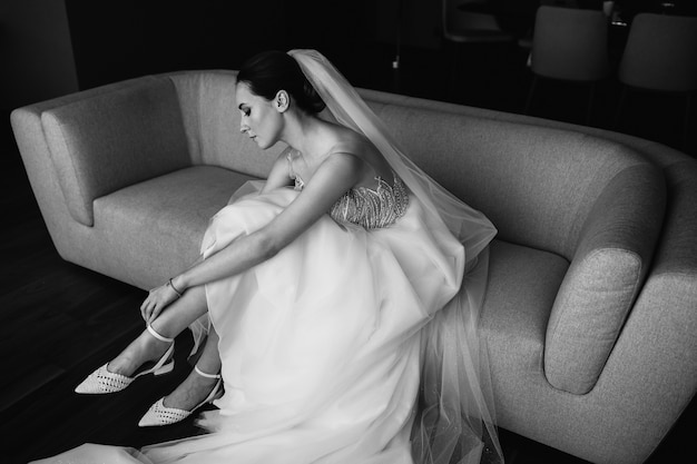 Bride putting her shoes on, sitting on a sofa.