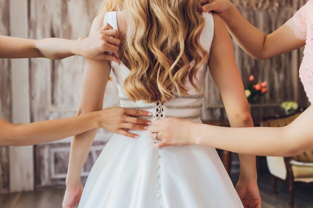 Bride putting on her white wedding dress. Wedding celebration concept. Beautiful lace wedding dress of the bride with open back.