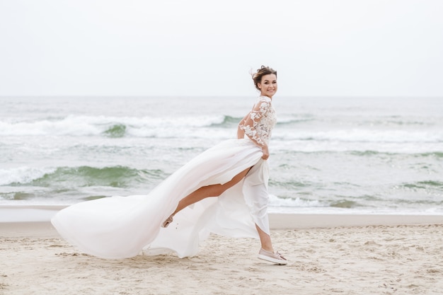 Bride runs along the sea beach on a cloudy day