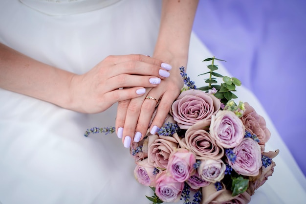 The bride's hands next to the bouquet on the background of the wedding dress