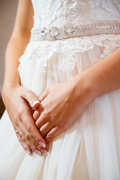 Le mani della sposa incrociate su un abito da sposa bianco
