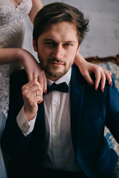 Photo bride's hands lie on the shoulders of the groom who looks at front