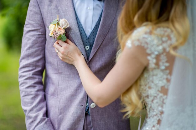 Bride's hands pinning a small boutonniere to a jacket for the groom Floral traditional decoration for groom an accessory on festive wedding suit Closeup