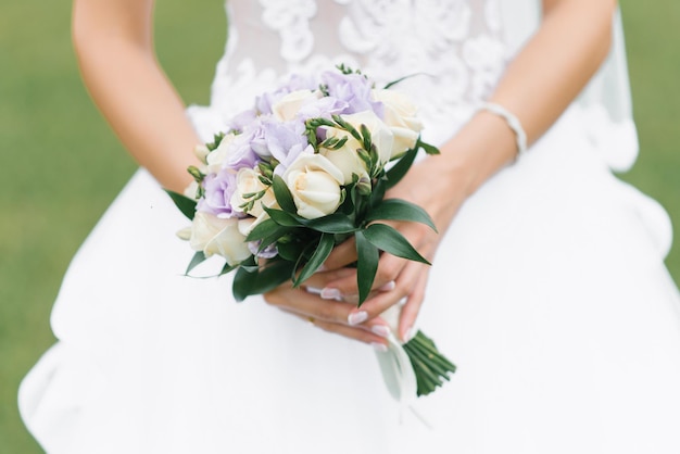 Il bouquet da sposa della sposa di rose latte e fiori lilla nelle mani della sposa