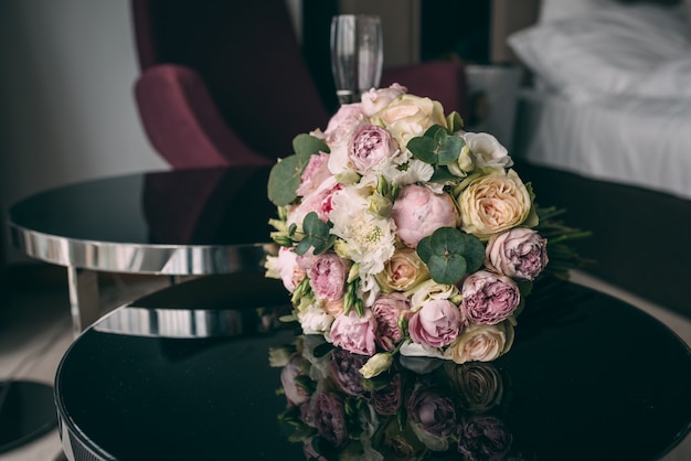The bride’s wedding bouquet in pink style lies on a black mirror table in the room