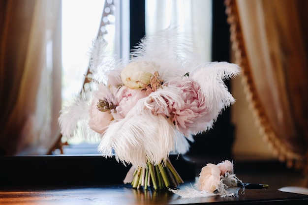 The bride's wedding bouquet of roses decorated with white feathers and a boutonniere