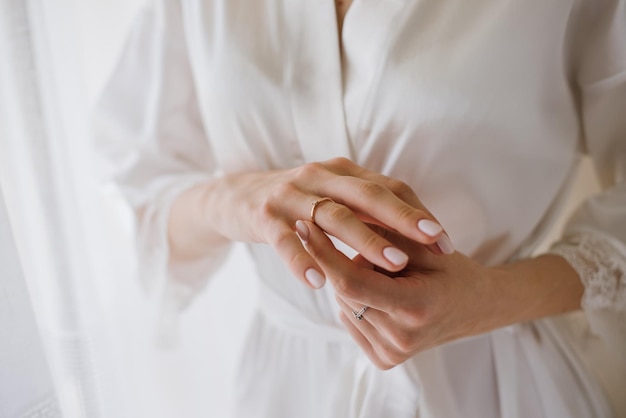 The bride in a silk robe in the morning with a ring on her\
finger