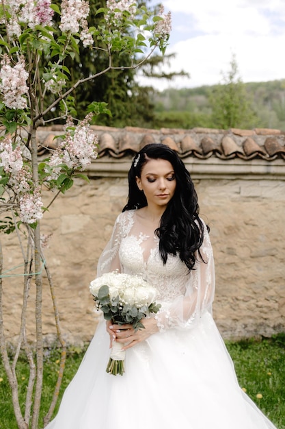 A bride sits in front of a wall with flowers.