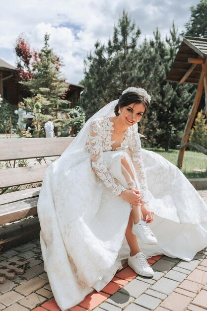 Foto la sposa seduta su una panchina si mette le scarpe da ginnastica bianche la sposa indossa scarpe da giubbotto bianche accessori da matrimonio