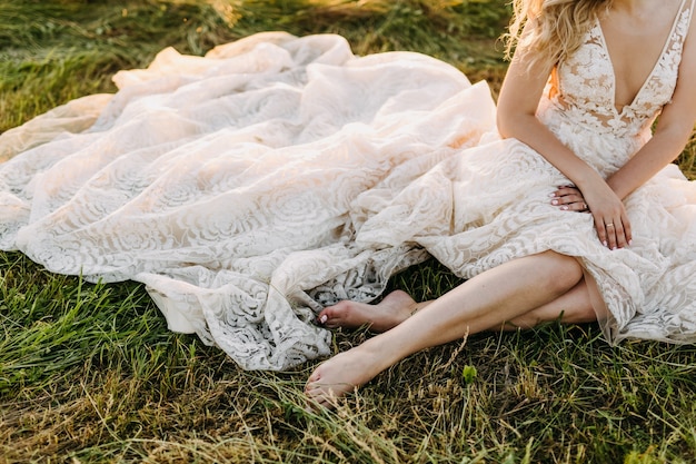 Bride sitting on grass, wearing a long wedding dress.