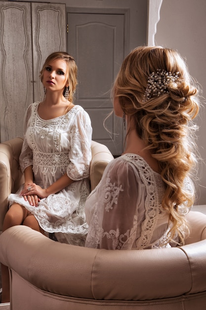 Bride sitting in white dress near the mirror