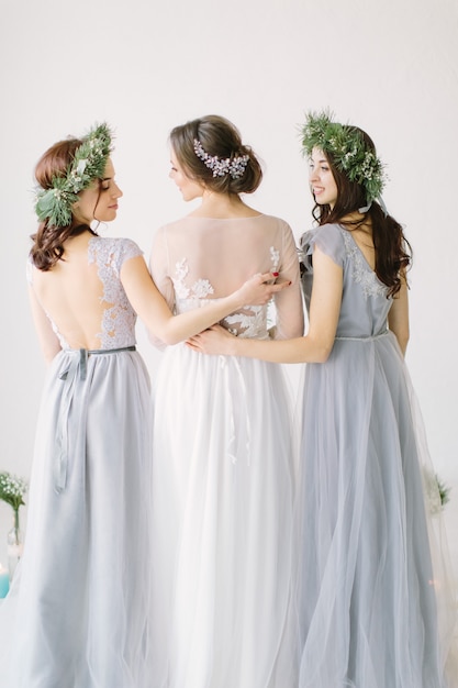 Bride standing with her back in a white wedding dress with two bridesmaids in blue dresses