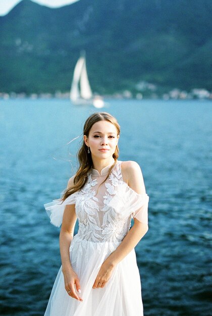 写真 花嫁は青い海と通過する帆船の背景に立っています