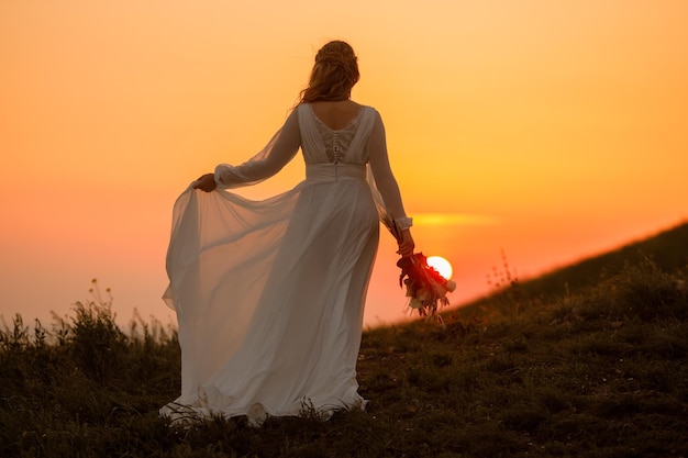 A bride stands in front of a sunset