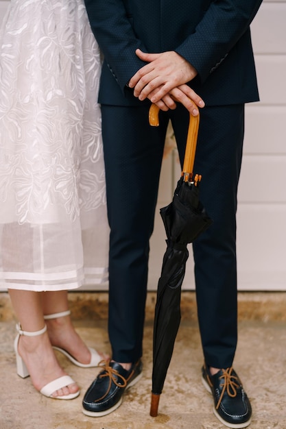 Bride stands next to the groom leaning on a wooden cane of a black umbrella closeup