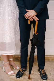 La sposa sta accanto allo sposo che si appoggia su una canna di legno di un primo piano nero dell'ombrello
