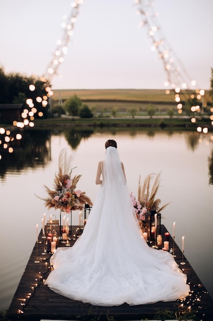 Невеста стоит на пирсе у озера на закате