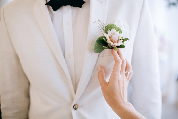 The bride touches the grooms boutonniere on a white jacket