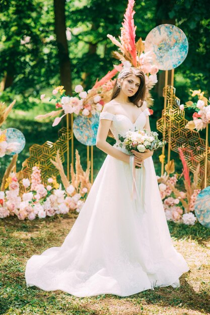 A bride in a traditional white dress with a wedding bouquet next to the wedding arch