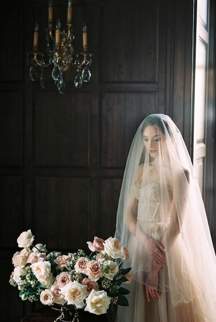 La sposa in un velo guarda un mazzo di fiori in un vaso sul tavolo