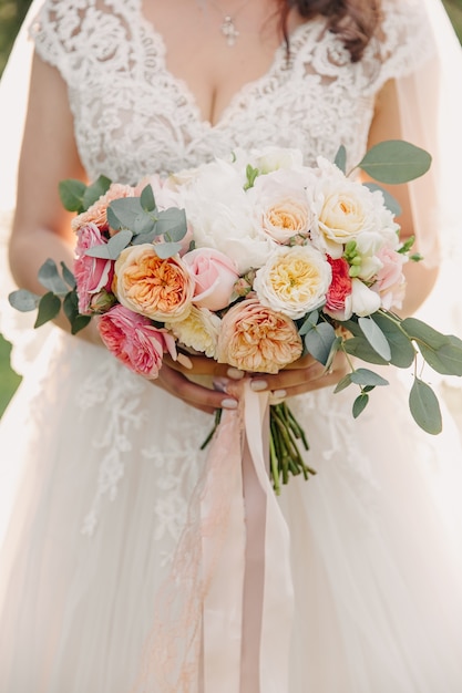 Bride wearing a lace white dress, holding her bridal bouquet made of various flowers.