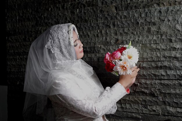 Фото Невеста в белом свадебном платье стоит у стены.