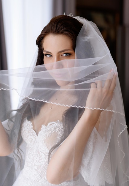 Bride in wedding dress holding veil near face