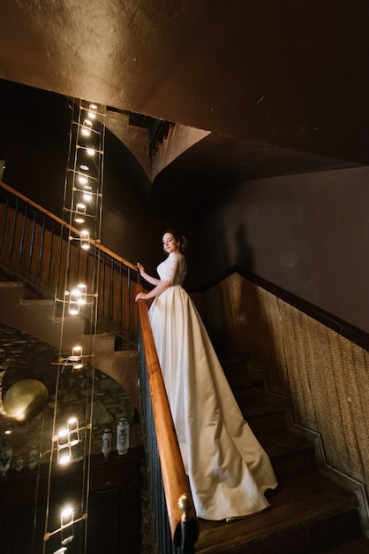 Невеста в свадебном платье стоит на деревянной лестнице