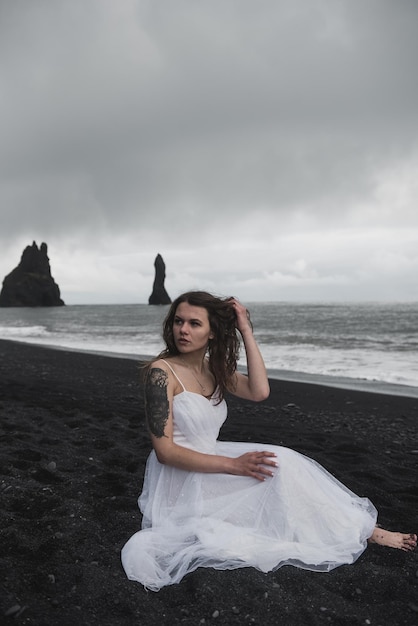 白い服を着た花嫁は、アイスランドの大西洋近くの黒い砂浜に立っています